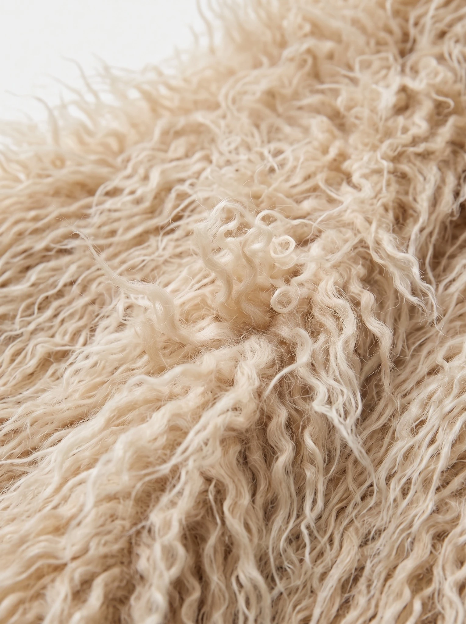 Close-up of soft beige shaggy faux fur fabric with long curly fibers.