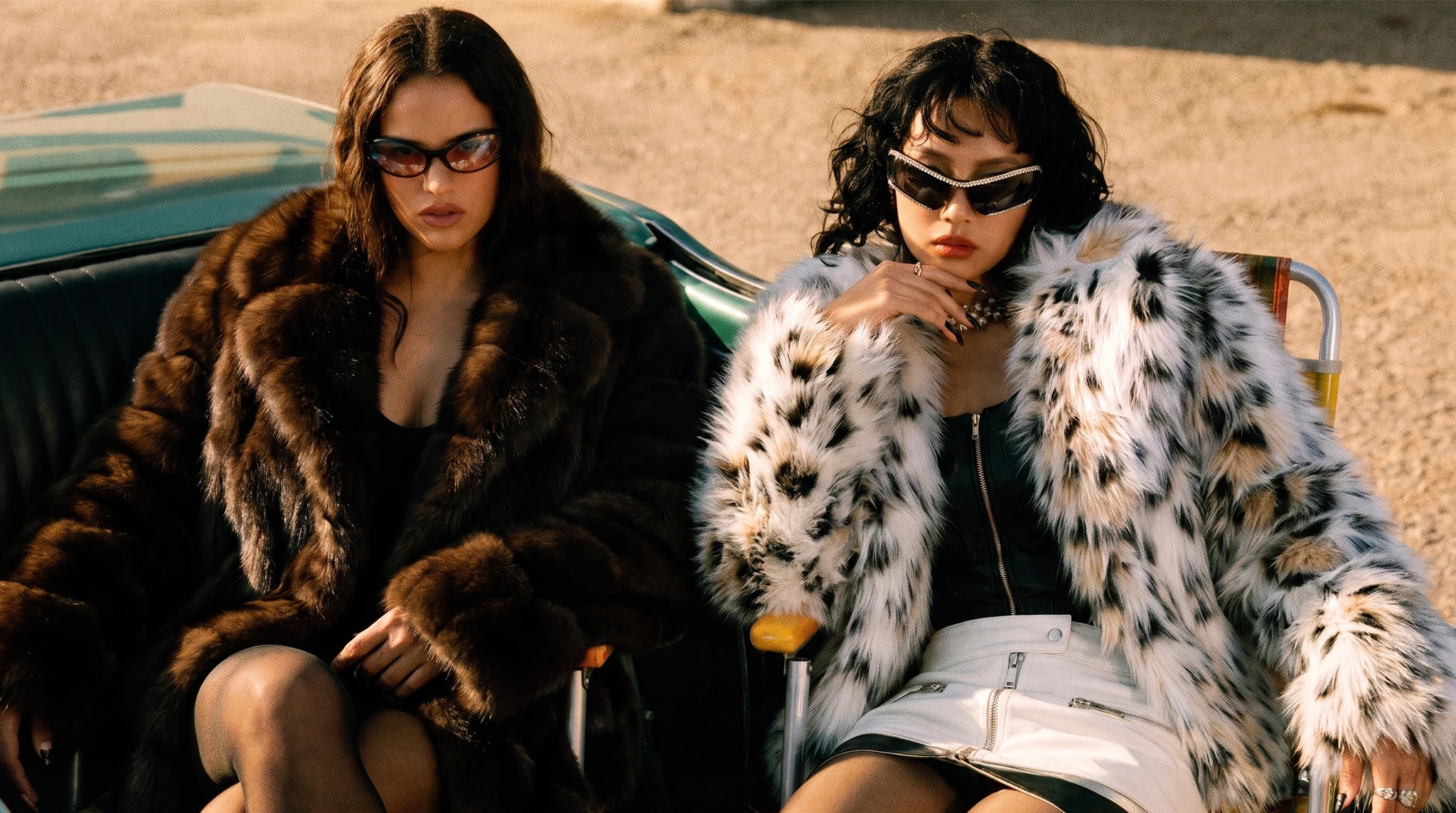 Two women wearing brown and spotted faux fur coats seated in a vintage car