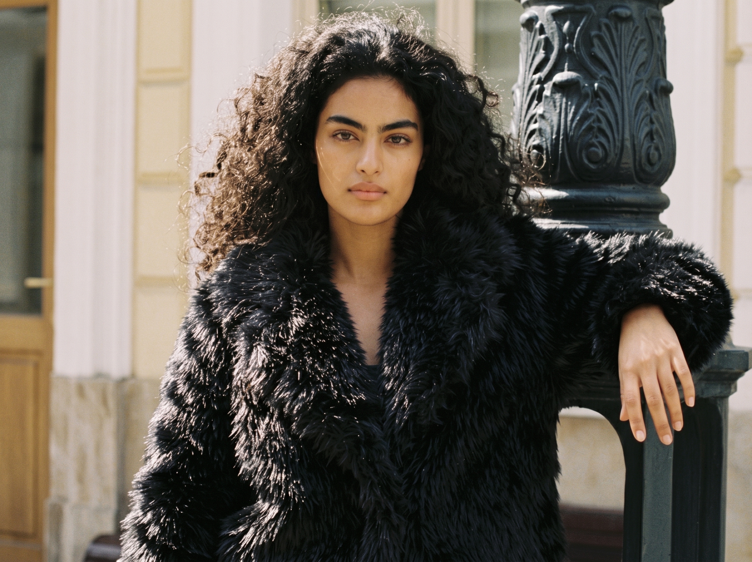 Woman wearing a black faux fur coat outdoors beside a decorative column