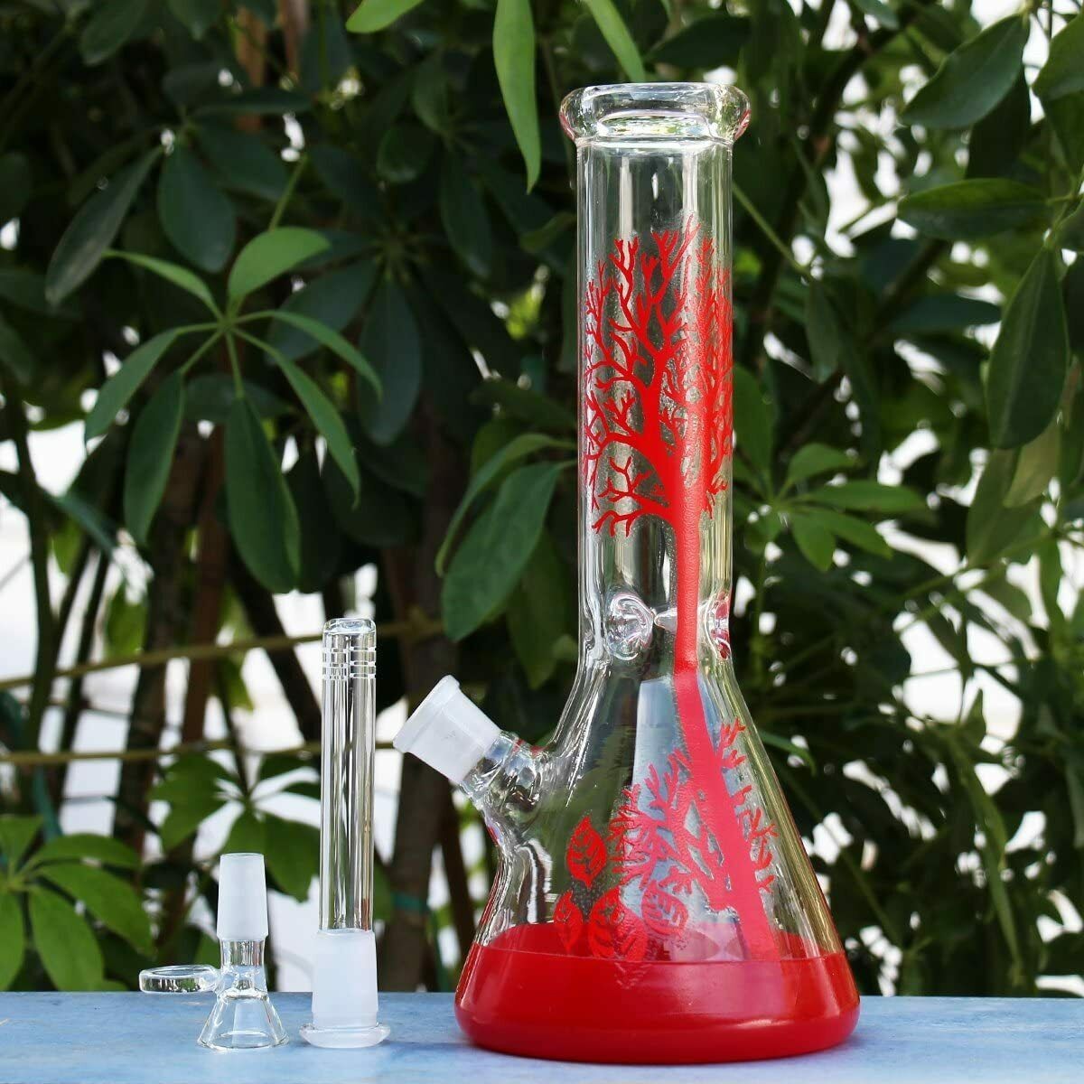Red tree pattern 10-inch beaker bong with downstem and bowl standing in front of green plants