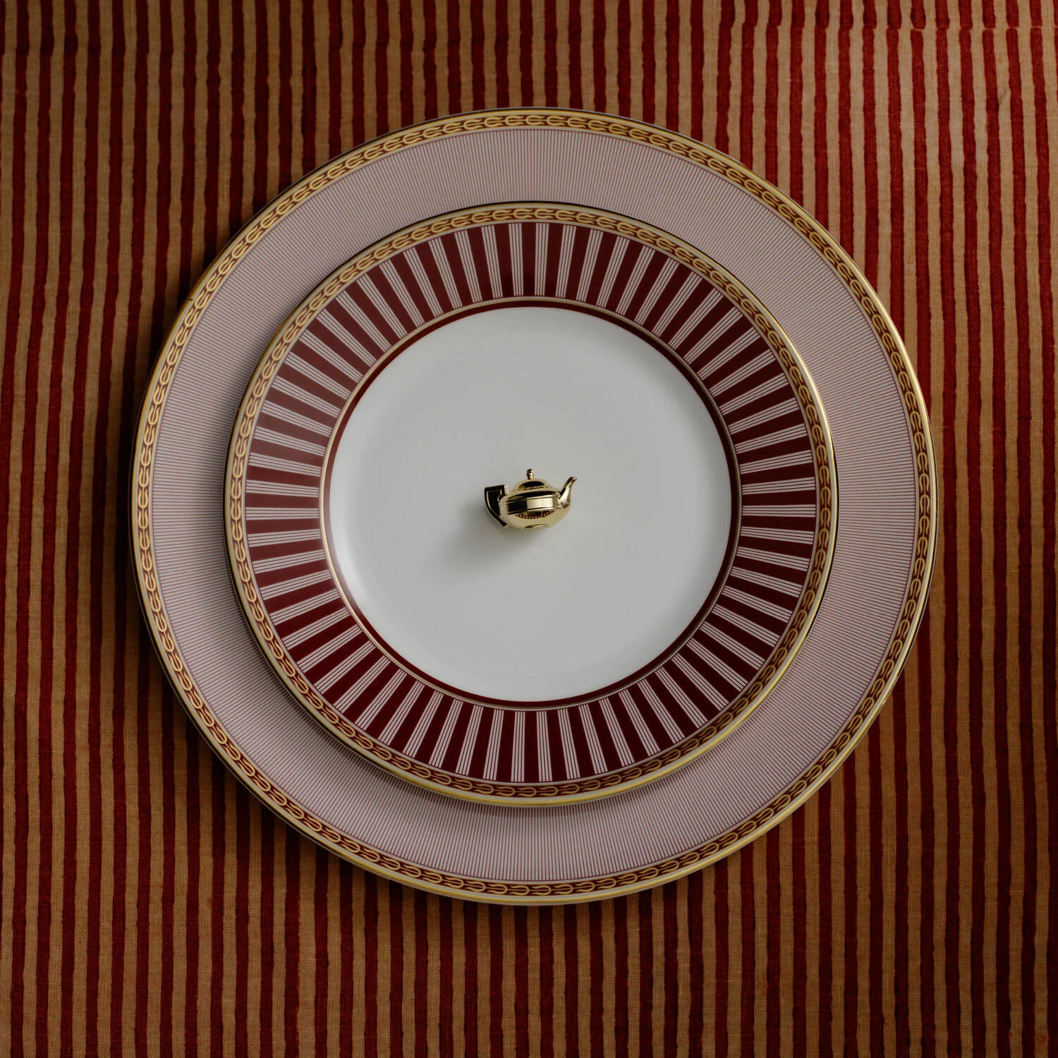 Splendour Red Dinner Plate - A set of three stacked Red Splendour ceramic plates, all set against a matching red and gold striped tablecloth.