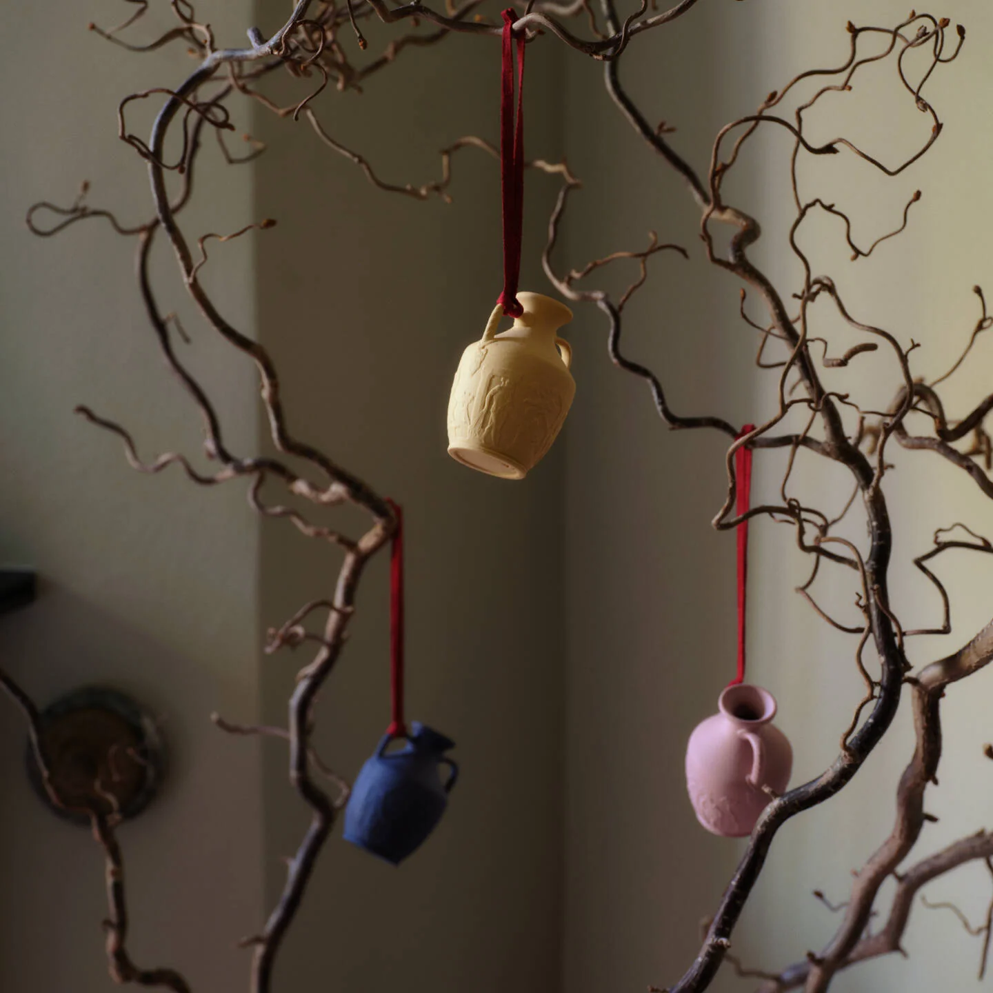 Mini Portland Vase  Pink - Three small hanging Wedgwood jasperware Portland vase cream, blue, and pink, suspended from red ribbons among bare brown branches against a muted indoor background.