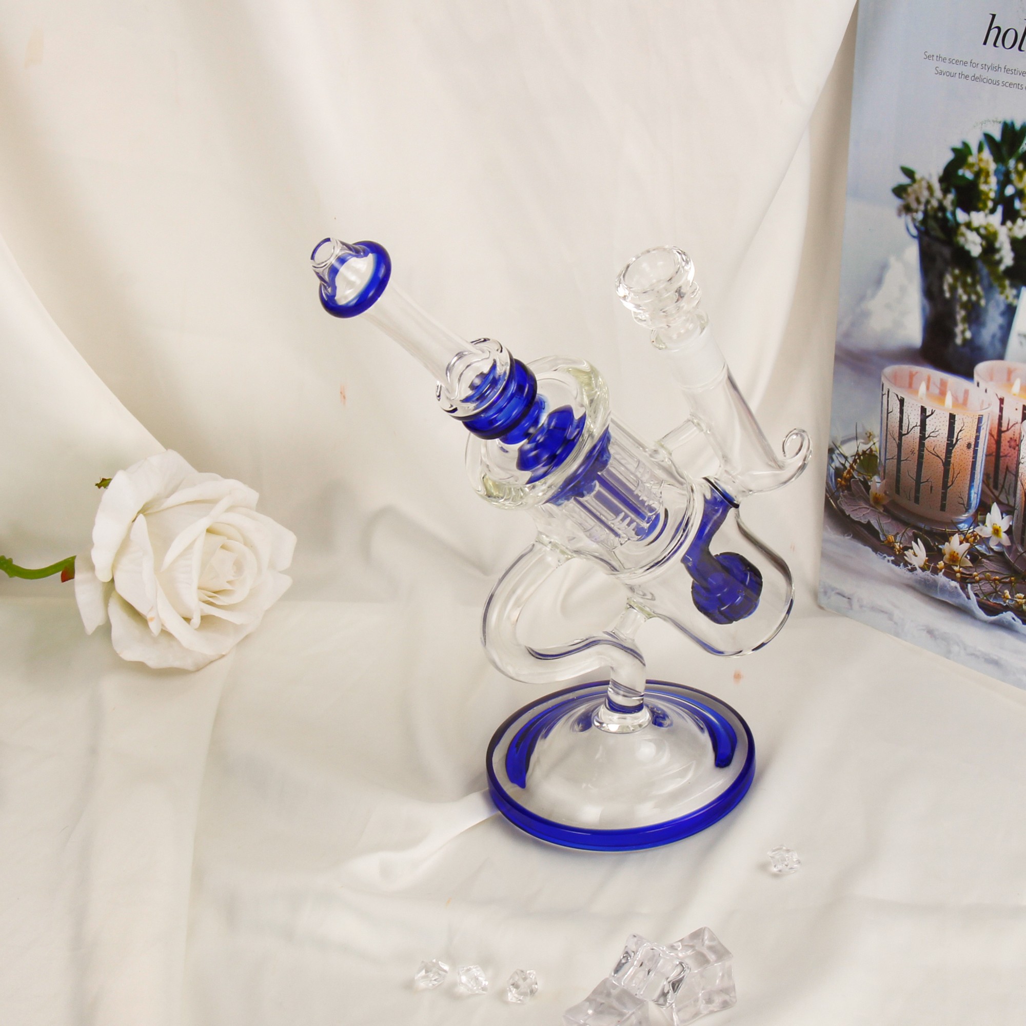 Blue recycler glass bong on white fabric with a white rose and candle behind it