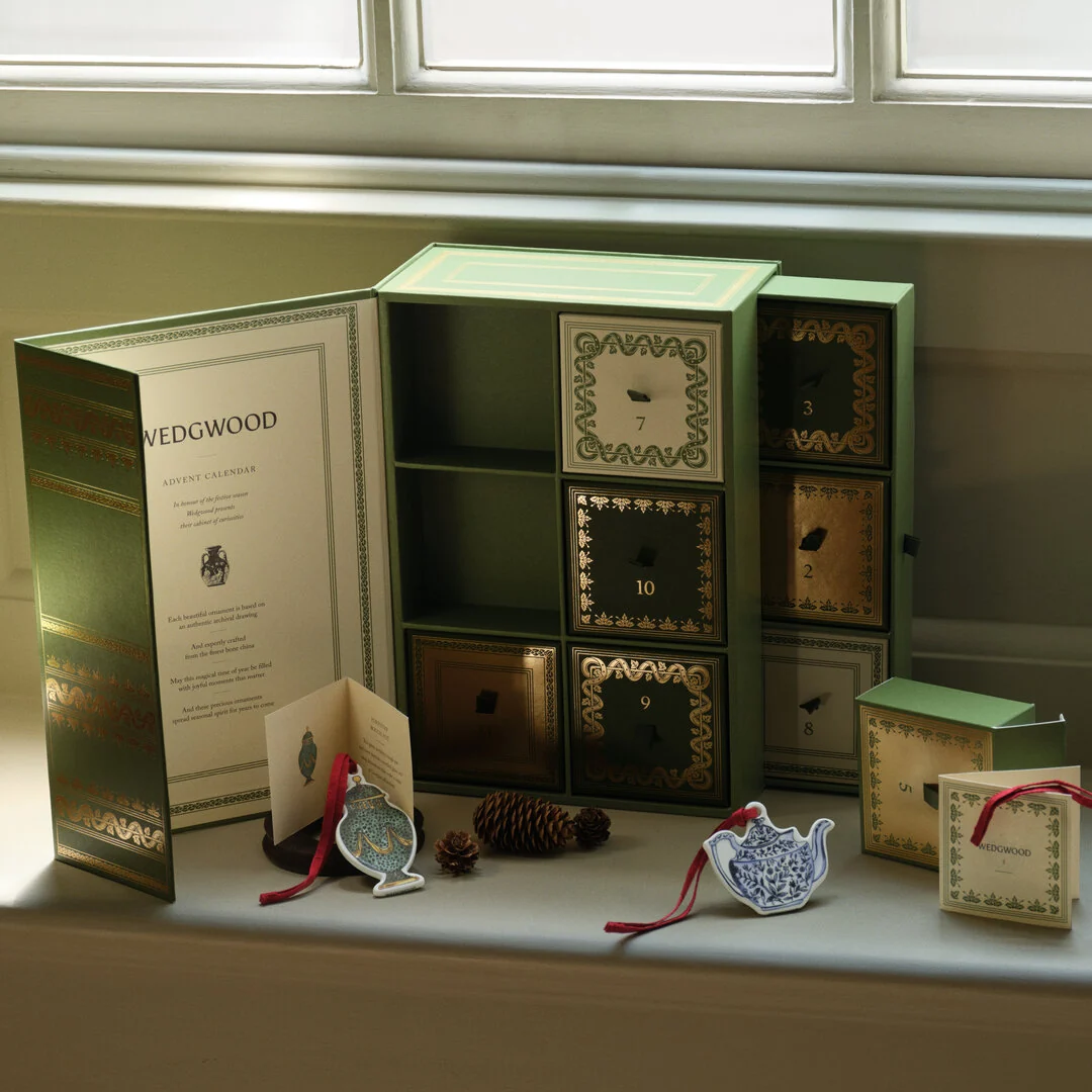 Archive Icons Advent Calendar - A Wedwood Christmas Advent calendar set displayed on a windowsill. The main product is a large sage green box with multiple small drawers decorated with gold patterns and numbered 1 through 24.