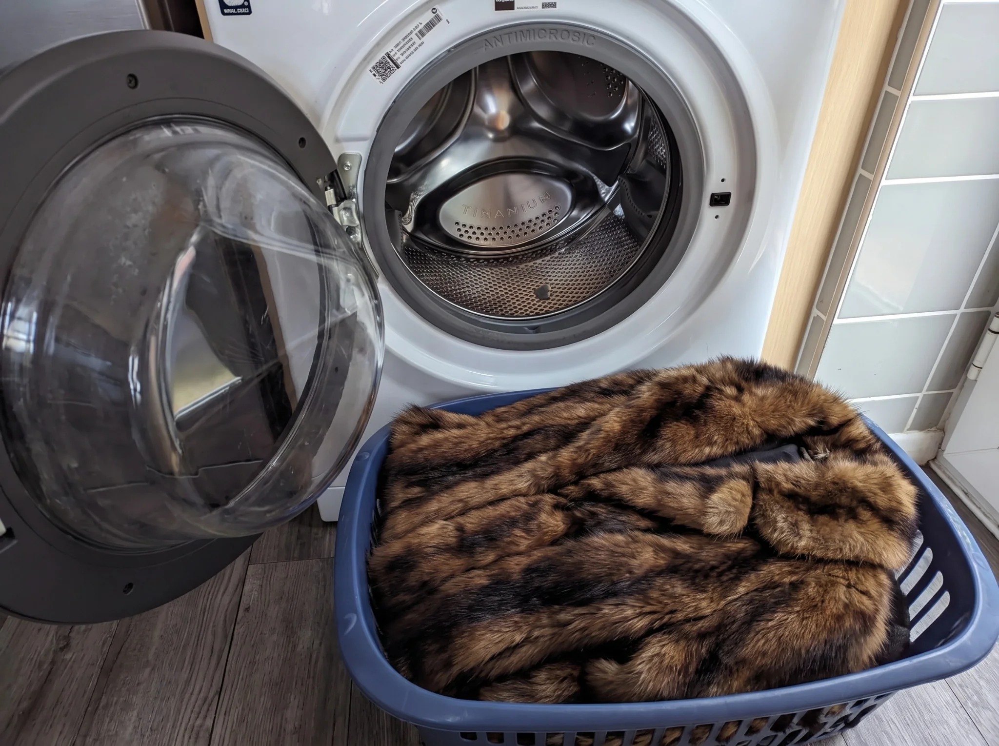 Brown fur coat in a laundry basket beside an open front-loading washing machine.