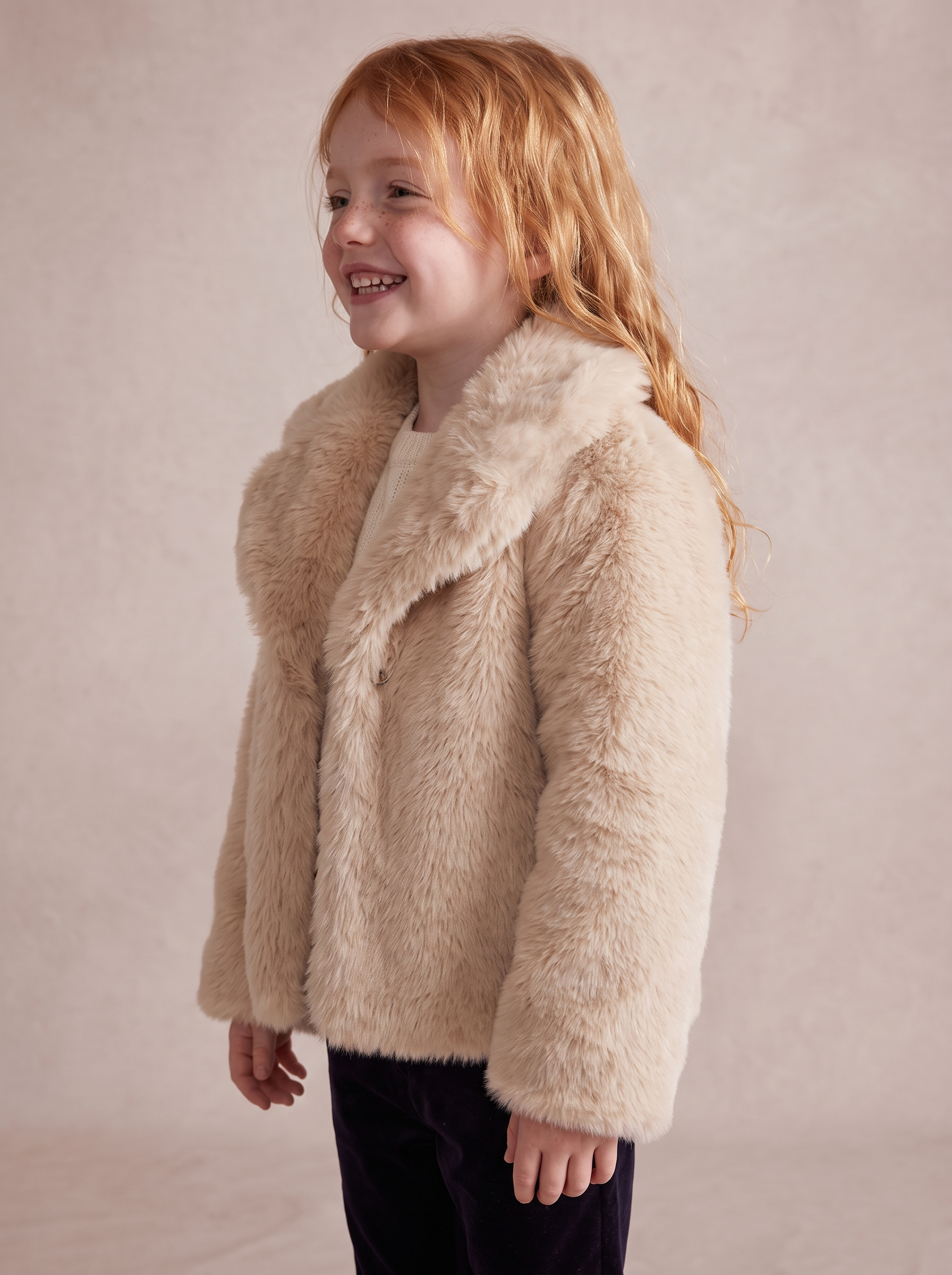 Girl smiling in a cream faux fur jacket, side view