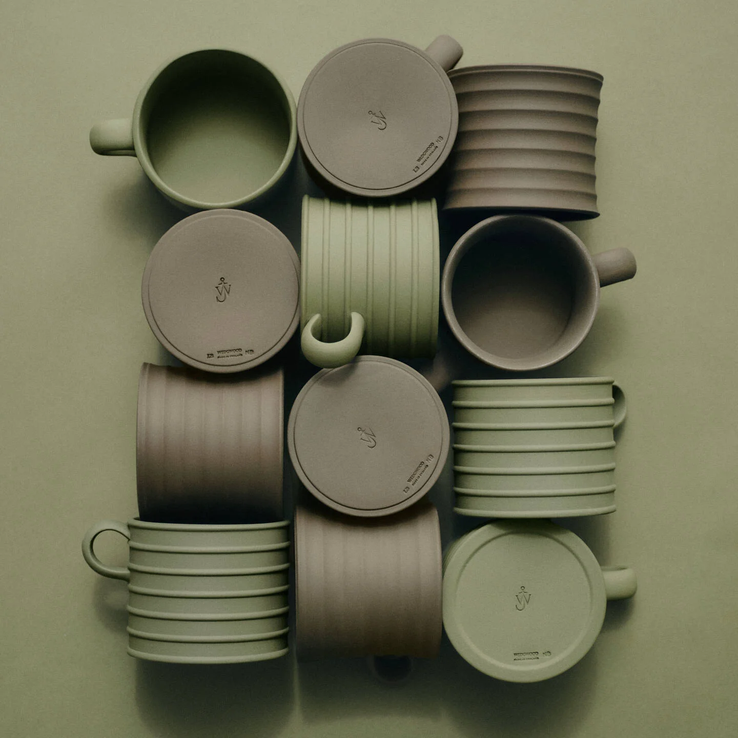 JW Anderson Mug Pair Marsh Green / Sage Green - A collection of JW Anderson jasperware mugs and matching lids arranged in a grid on a solid sage green background. The set features two primary colors: a muted sage green and a taupe-brown.