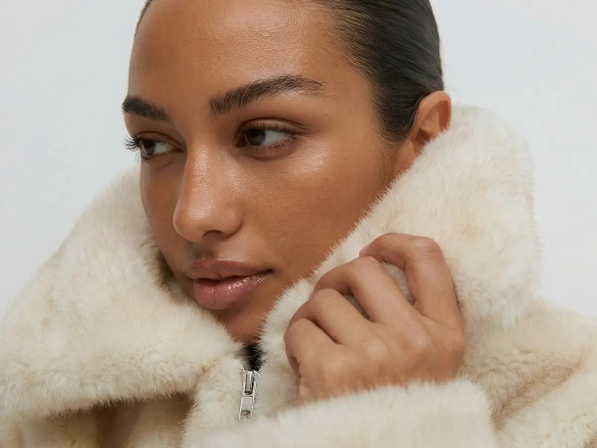 Adult woman wearing a cream faux fur coat in a natural indoor portrait