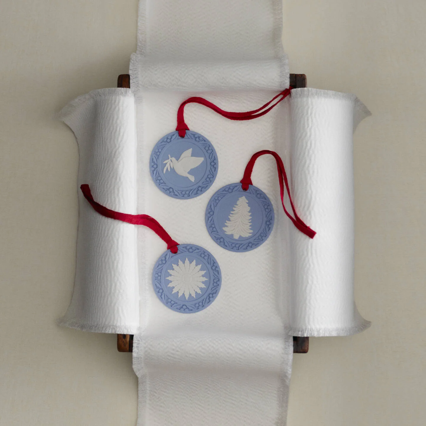 Christmas Tree Ornament Blue - Three round Wedgwood jasperware blue and white decorative hanging ornaments with red hanging strings, displayed on a white paper towel roll holder against a light beige wall.