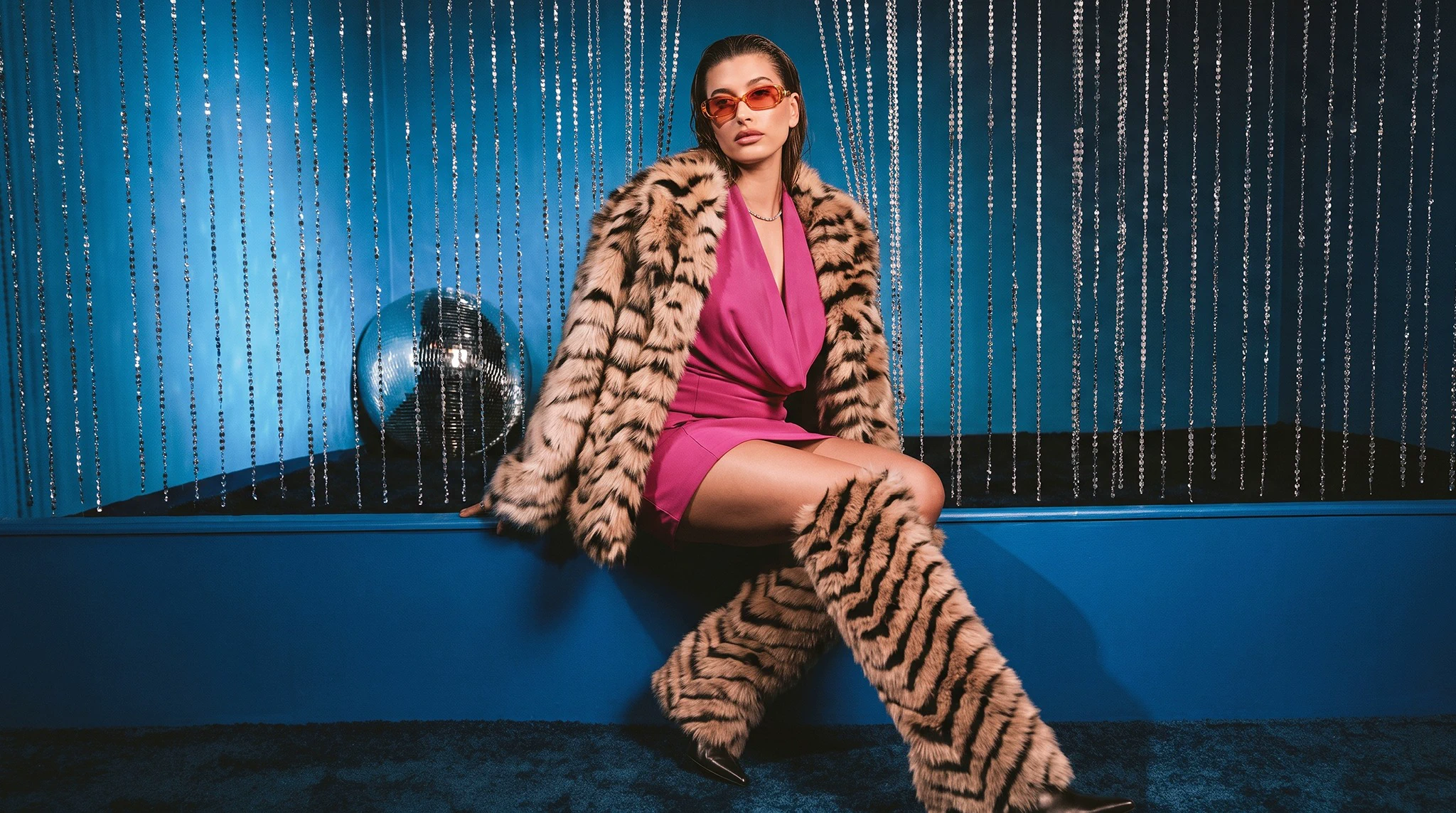 Woman wearing a tiger-print faux fur coat over a pink dress in a blue lounge